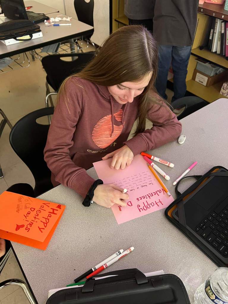 Student writing out their Valentine Project on pink paper