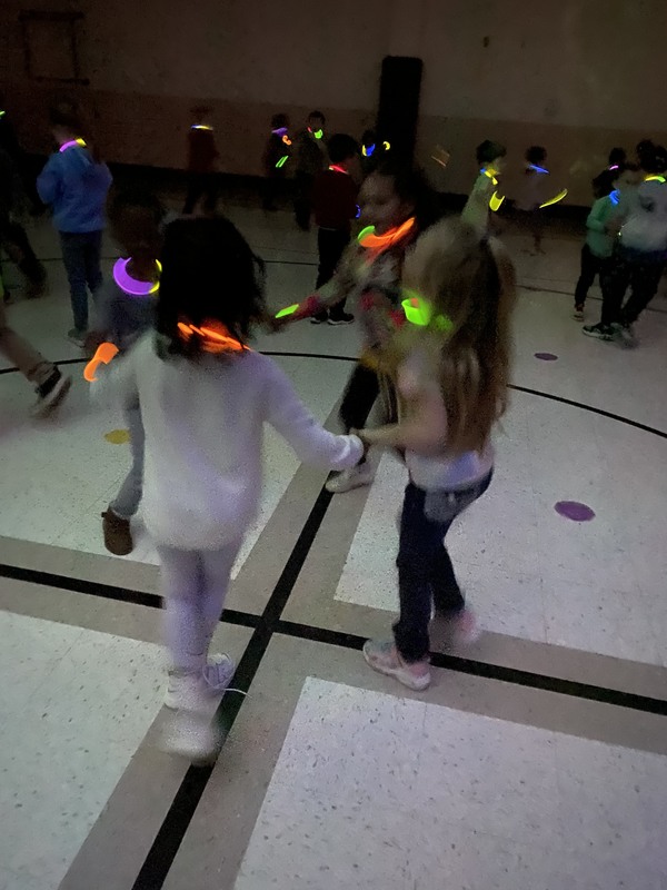 Students holding hands dancing in the gym with glowing necklaces and bracelets